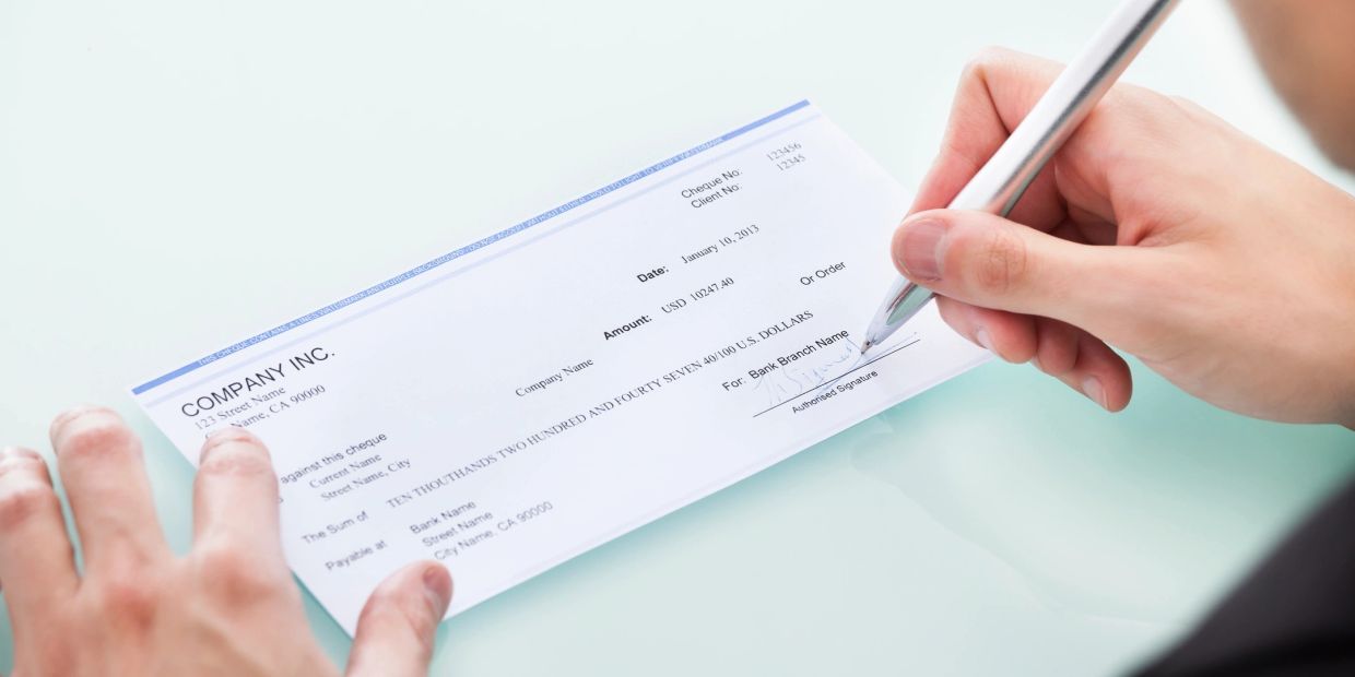 Person signing a company check with a pen.