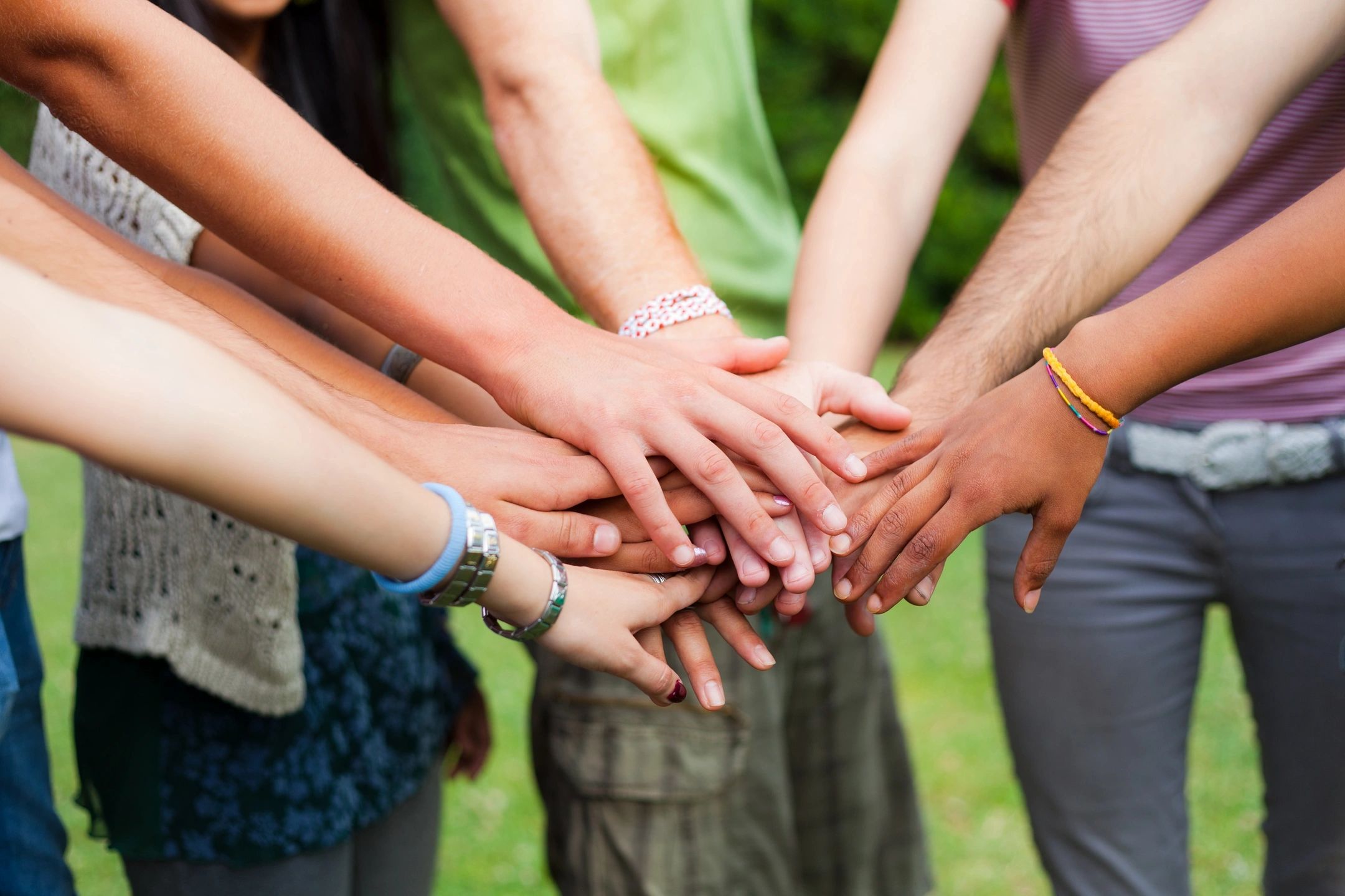A group of people of different races and genders with their hands stacked together in the middle.