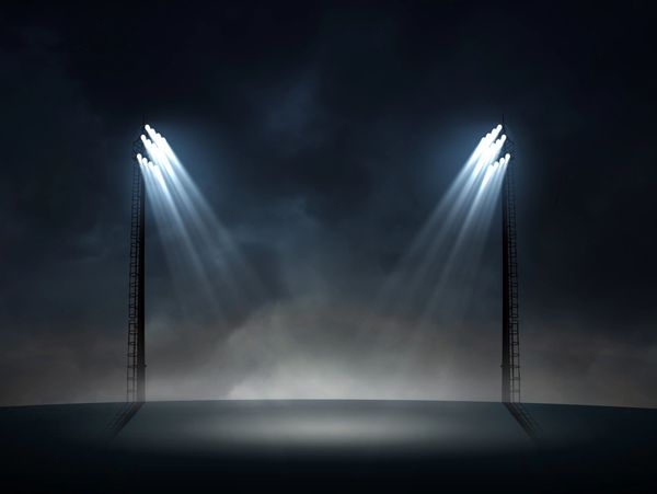 Two tall floodlights shining bright in a dark, foggy environment.