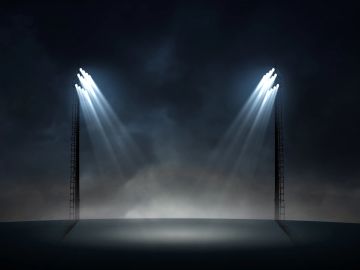 Two stadium floodlights shining brightly in a foggy night.
