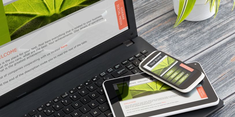 Laptop, tablet, and smartphone displaying a green-themed business website on a wooden table.