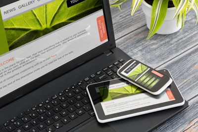 Desk with laptop, tablet and cell phone. Potted plant.