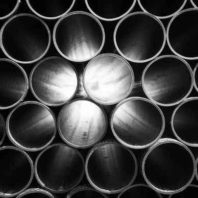 Stacked metal pipes reflecting light, arranged in a circular pattern.