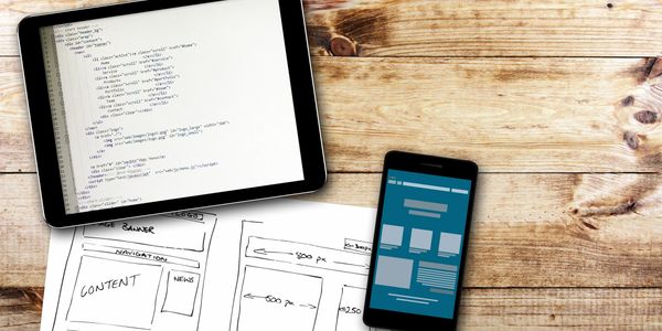 Computer tablet showing computer HTML code, hand-written plans for web page design and smartphone.