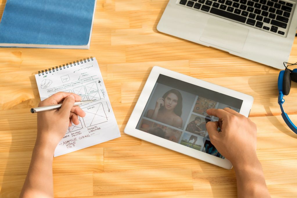 Person sketching web design while browsing images on a tablet.
