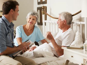 Doctor consulting elderly couple at home, taking notes.