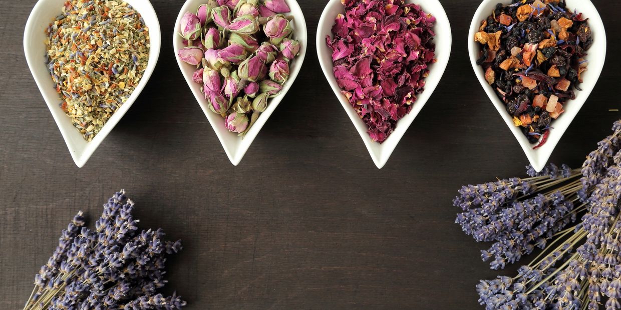 Four white dishes with various dried herbs and flowers on a wooden surface.