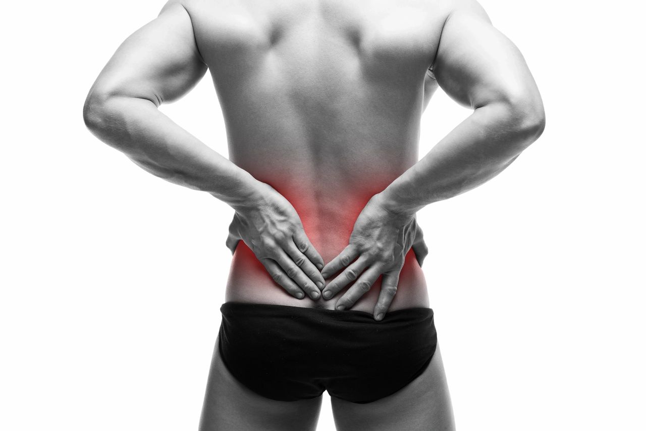 Man with back pain, his hands on his lower spine, wearing black slips
