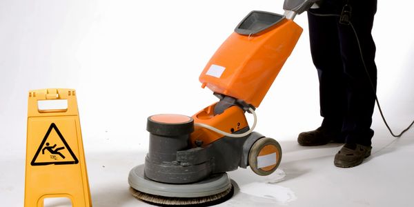 A man with a orange floor scrubbing machine and a caution sign 