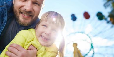 Father and daughter smiling with a ferris wheel in the background.