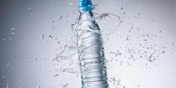 A plastic water bottle splashing water around it against a light background.