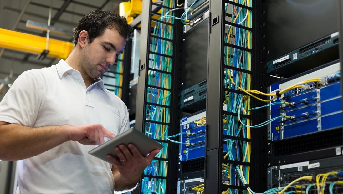 Technician working in a server room with cables and equipment.