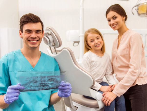Dentist showing dental x-ray with smiling mother and child in clinic.