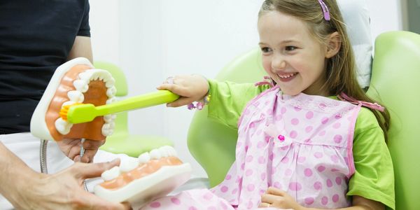 Smiling girl at dental office brushing a tooth model.