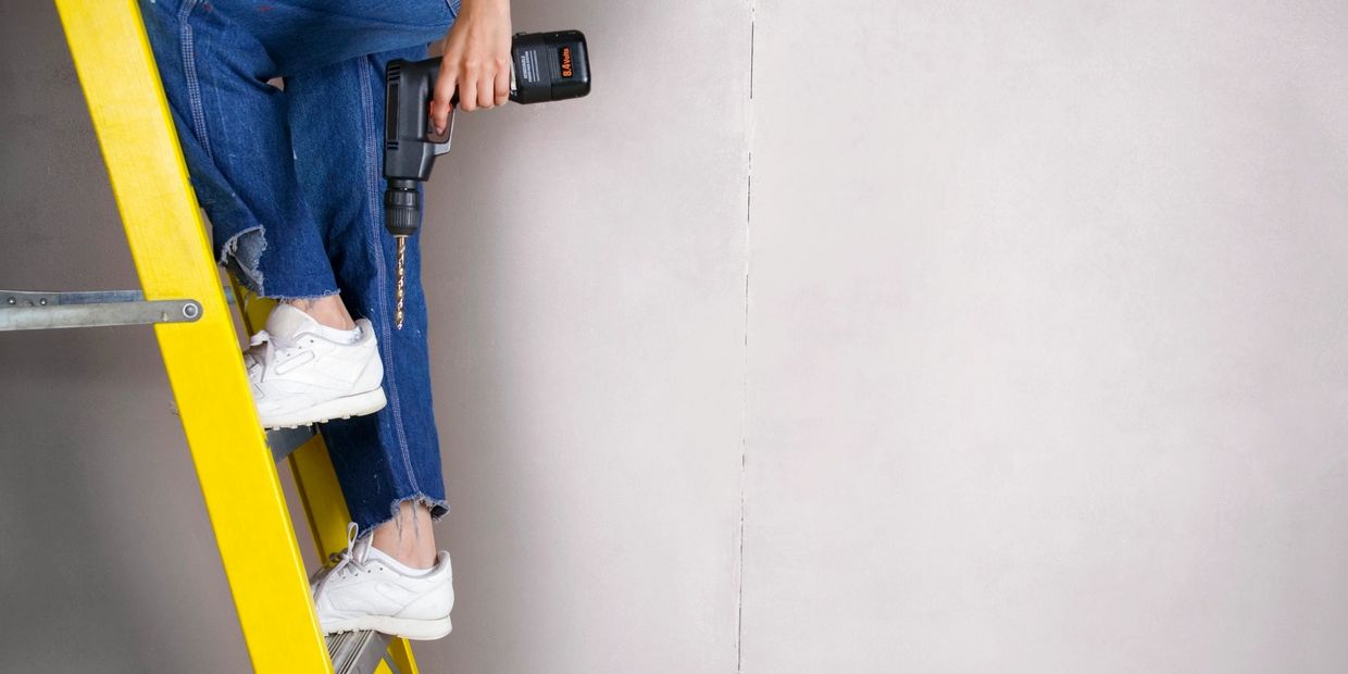 Person standing on a yellow ladder holding a drill.