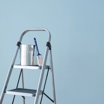 a ladder with a paint bucket and brush on it