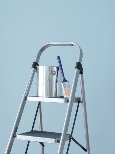 Step ladder with paint can and brush against a blue wall.