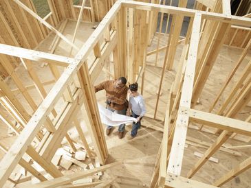 Arial view of two people reviewing building  plans amid exposed wood framing in a building