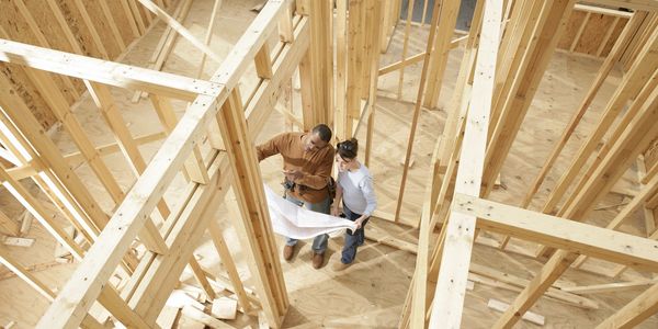 Two people reading blueprints in a house under construction