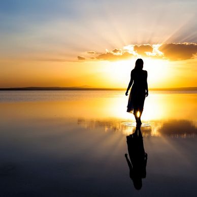 Silhouette of a woman walking on water during a golden sunset.