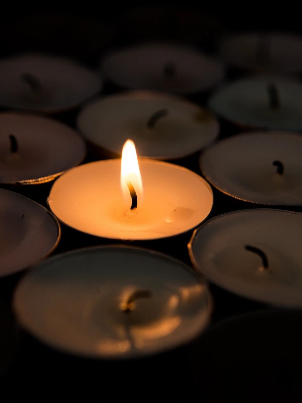 One lit candle among many unlit candles in the dark.