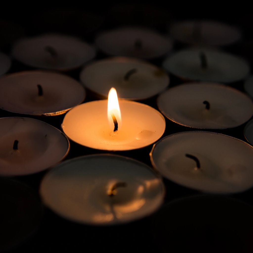 One lit candle among many unlit candles in the dark.