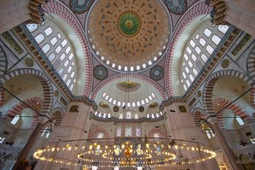 Intricate ceiling and dome inside a grand mosque with hanging lights.