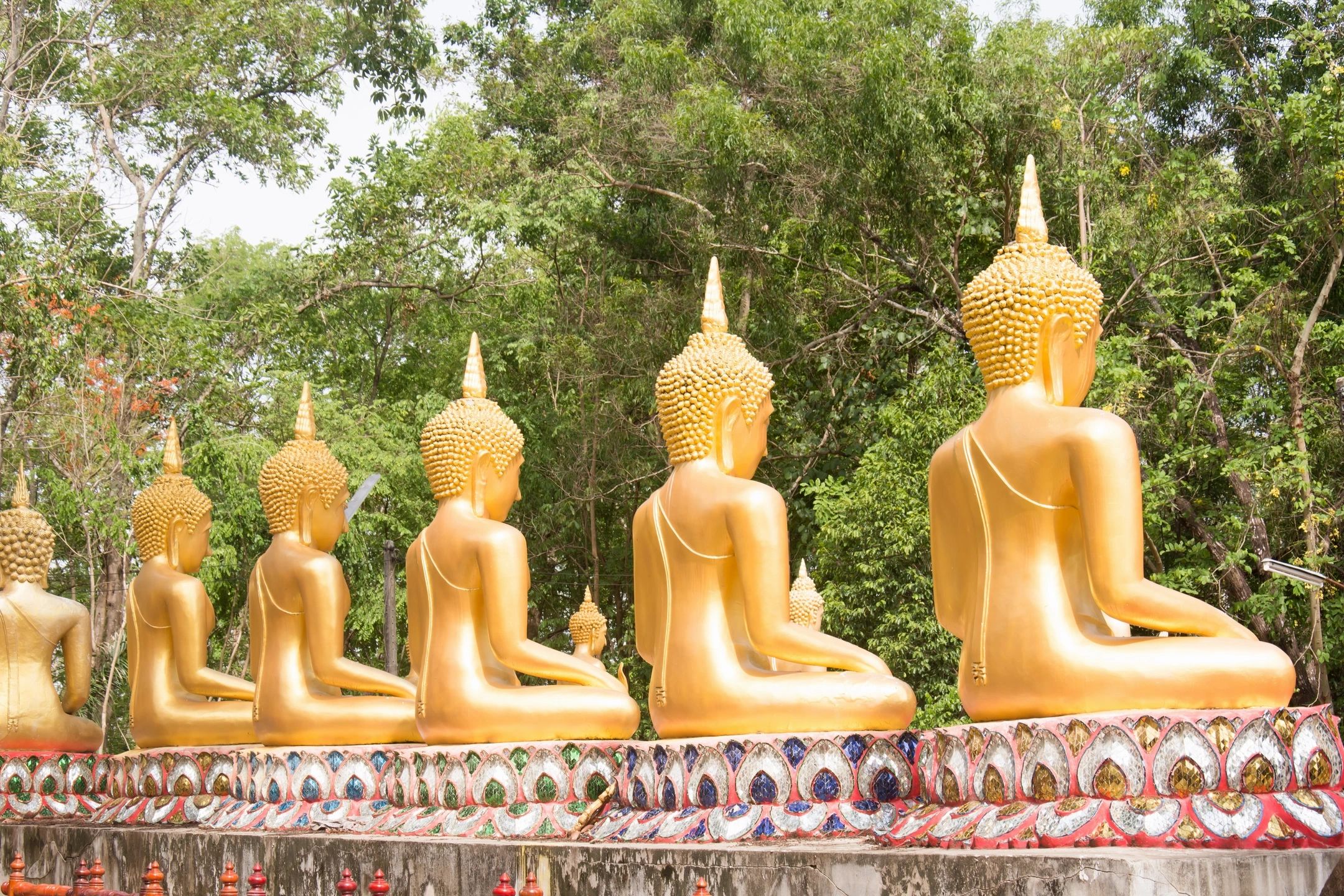 Row of golden Buddha statues in a lush garden setting.