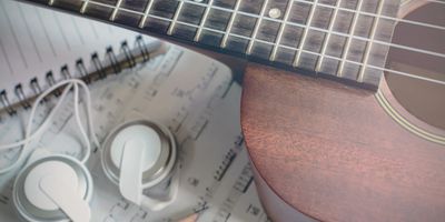 Close-up of a ukulele, earphones, and sheet music on a desk.