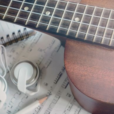 Guitar neck, headphones, pencil, and sheet music arranged together.