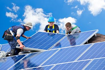 Three workers install solar panels on a rooftop under a blue sky.