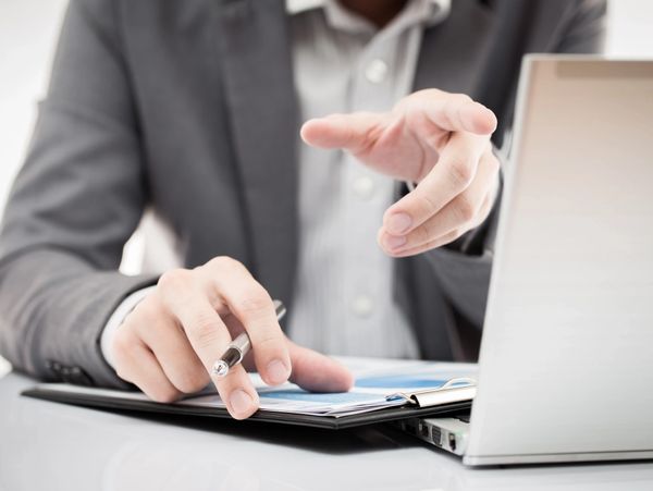 Businessperson reviewing documents and pointing at data on a clipboard.