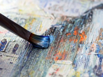 Close-up of a paintbrush applying blue paint on a textured canvas.