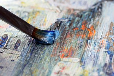 Close-up of a brush painting blue on a textured canvas.