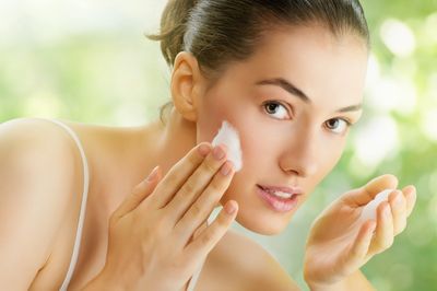 Young woman applying cream on her face in a bright setting.