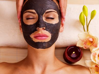 Woman relaxing with a black facial mask and a calming spa setup.