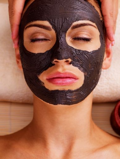 Woman relaxing with a dark facial mask in a spa setting.