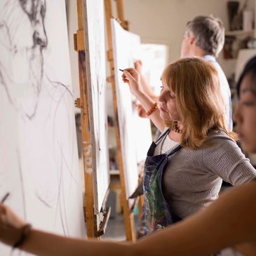 People focused on drawing sketches on canvases in an art class.