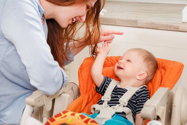 Mother smiling and interacting with her happy baby in a high chair.