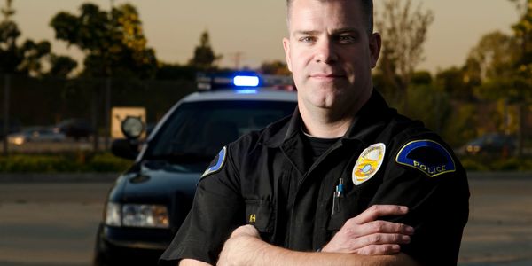 Confident police officer standing in front of a patrol car with flashing lights.