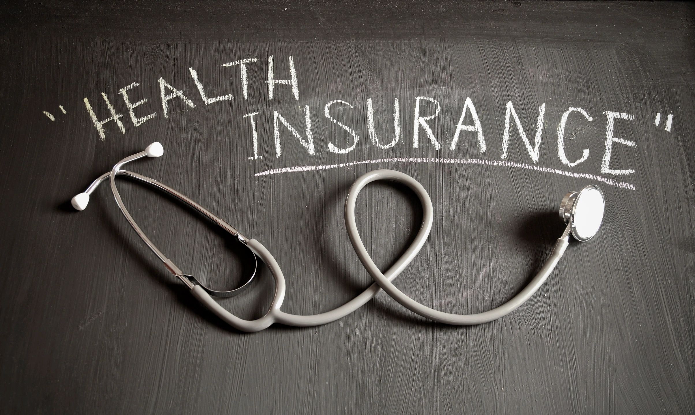 Picture of chalkboard with words, "Health Insurance" written on it with a stethoscope under words. 