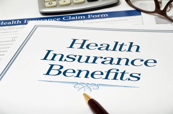 Close-up of health insurance benefits document and claim form with pen and glasses.