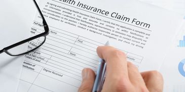 A person filling out a health insurance claim form with glasses nearby.
