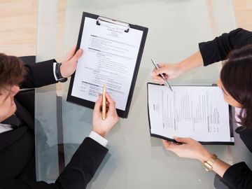 Overhead photo of 2 persons sitting at table in business meeting setting reviewing paperwork 