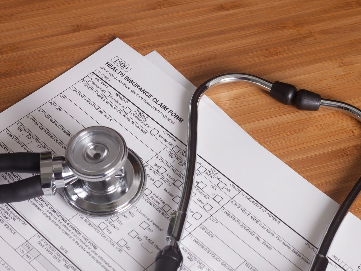 Stethoscope resting on a health insurance claim form on a wooden desk.
