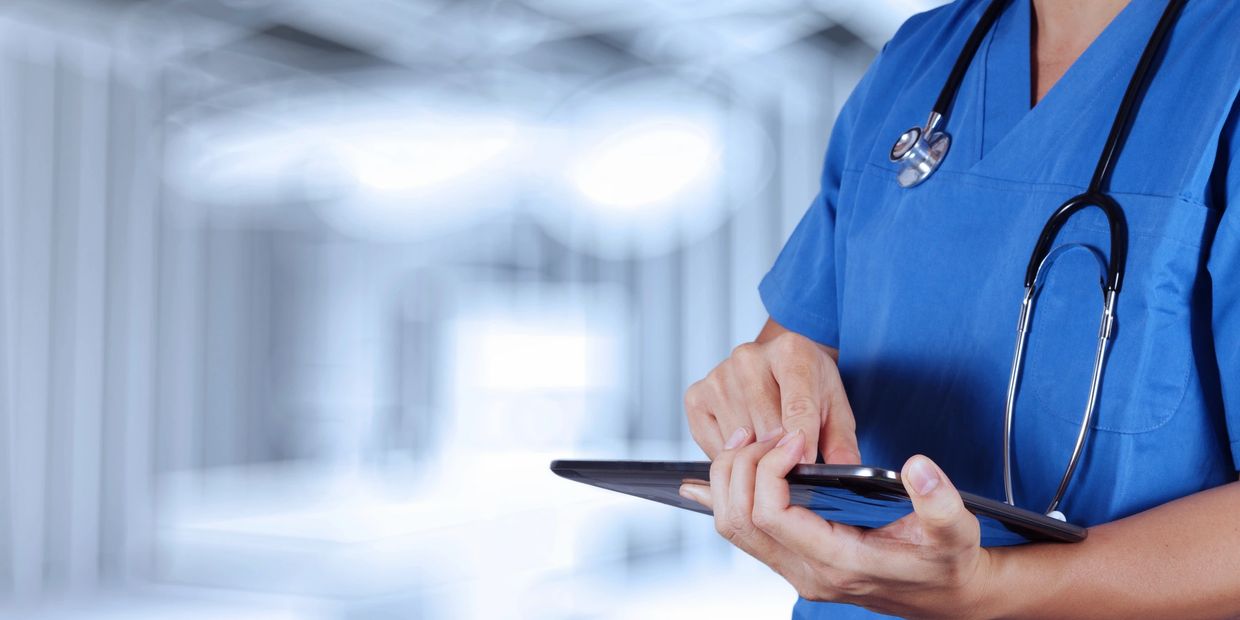 Healthcare professional using a tablet in a hospital corridor.
