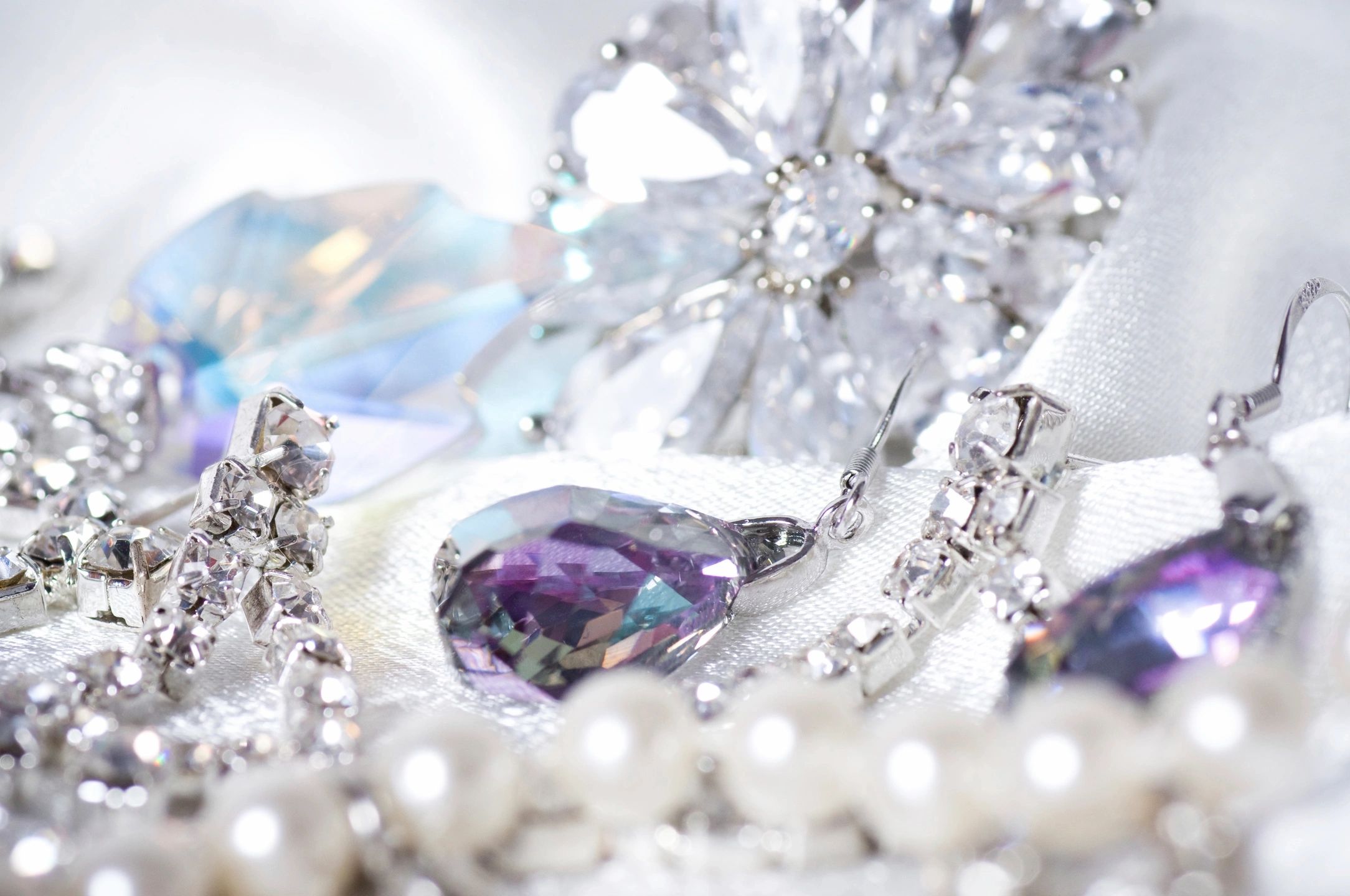 Assortment of diamond, pearl, and purple gemstone jewelry displayed on white fabric.