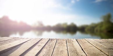 Sunny wooden deck with a blurred lake and trees in the background.