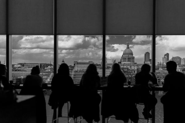 Silhouettes of people sitting by large windows with city view.