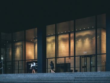 Two people walking past a modern glass building at night.